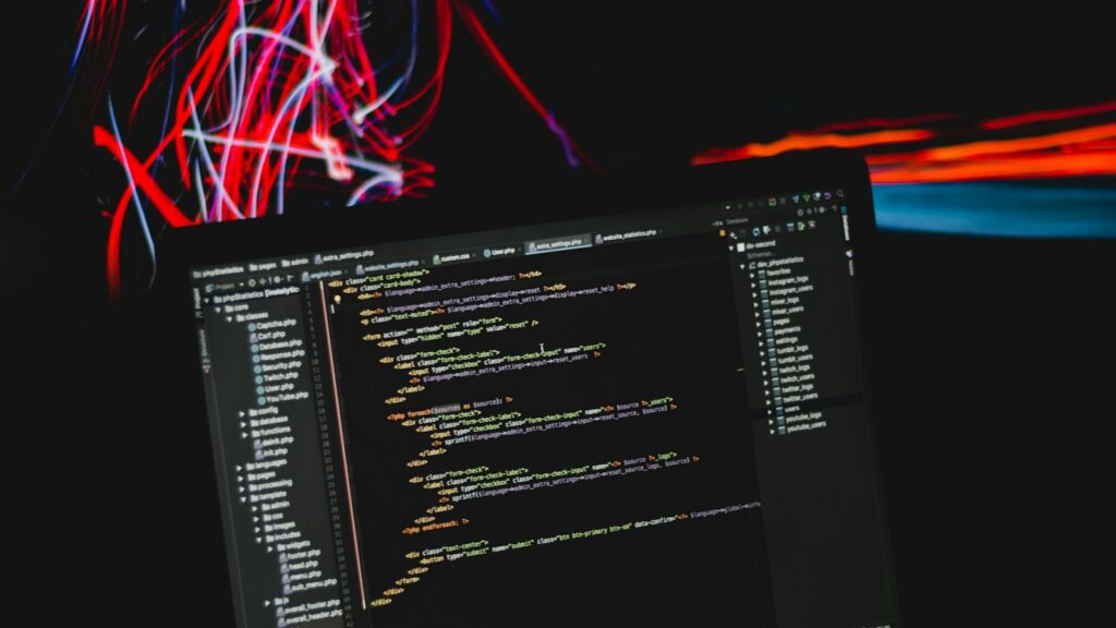 Laptop mit Programmcode vor bunten Lichtspuren – kostenlose Software